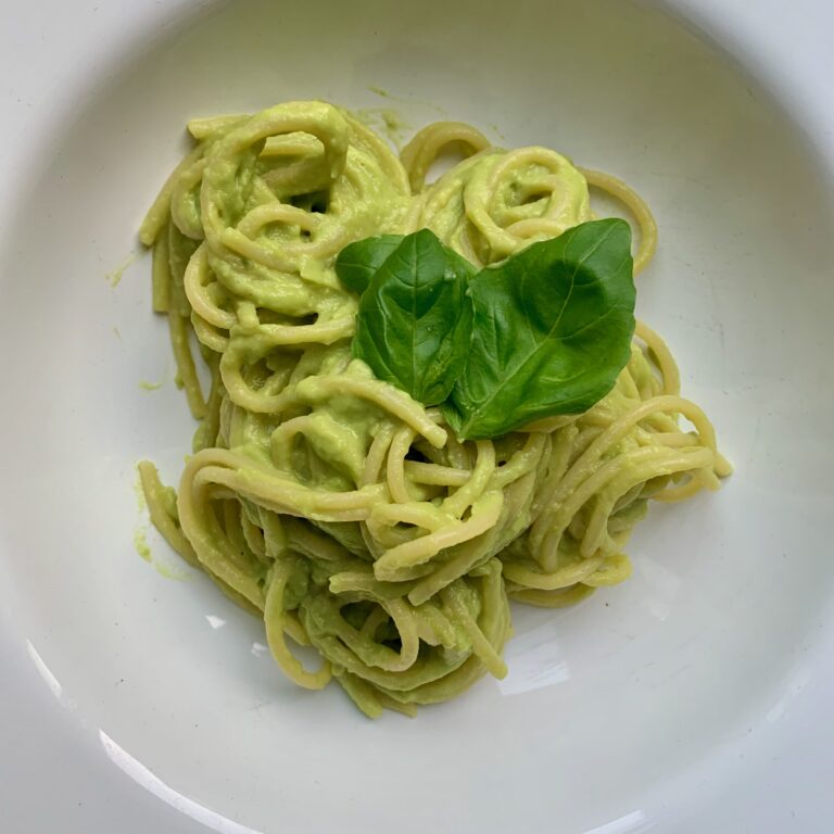 Een bord met romige avocado pasta, klaar om geserveerd te worden, met een frisse, groene saus.